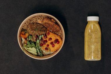 A vibrant vegan bowl with quinoa, fresh vegetables, and a smoothie bottle against a dark backdrop.